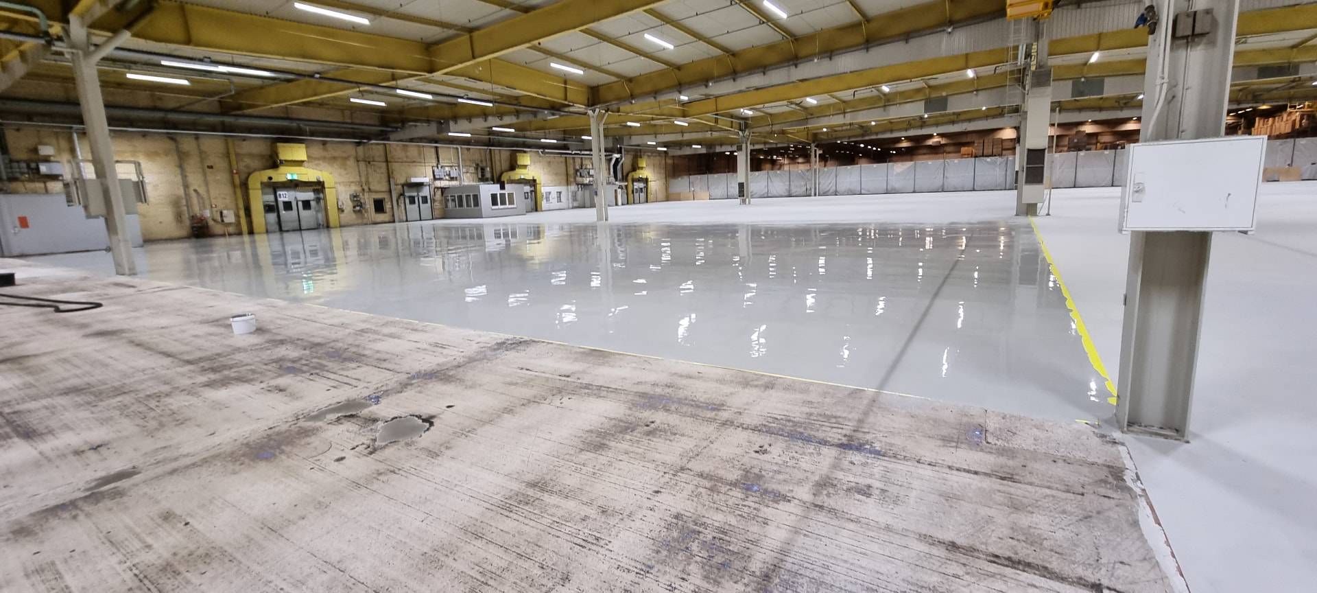 Freshly poured seamless silicate floor meeting raw concrete substrate in an industrial warehouse hall